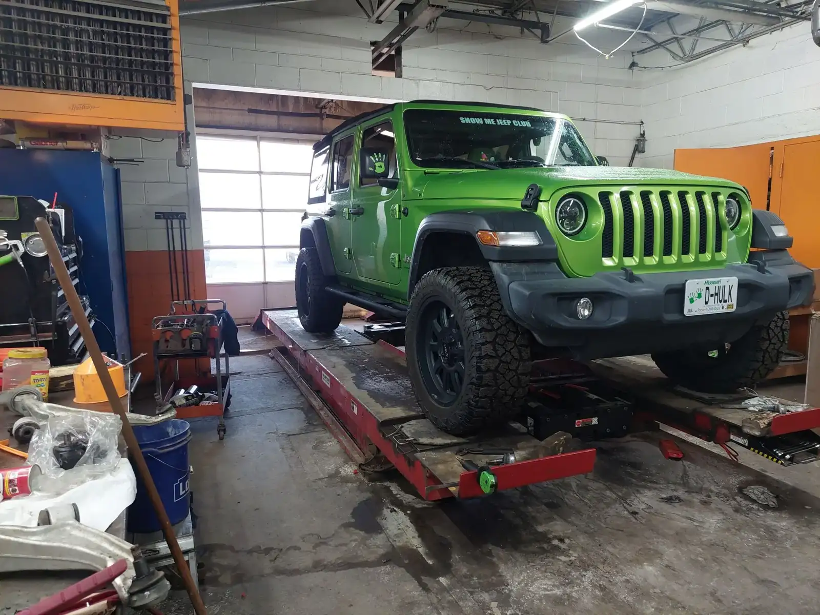 A green Jeep Wrangler on the alignment rack inside the shop