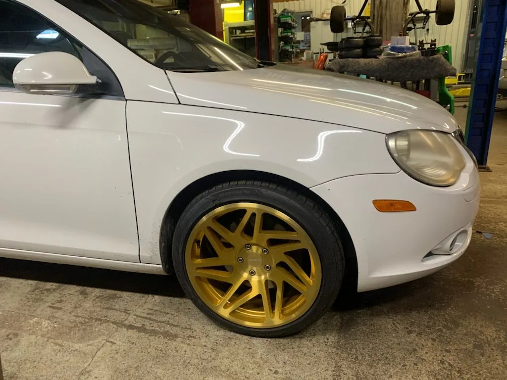 A white sedan with gold wheels inside the shop